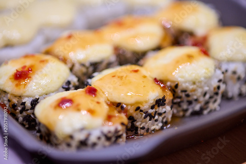 Fotografie Creamy baked sushi rolls with spicy sauce and black sesame seeds closeup on serv