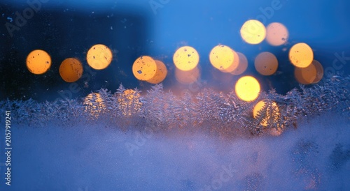 Frosty windowpane with blurred golden lights, a cold winter evening