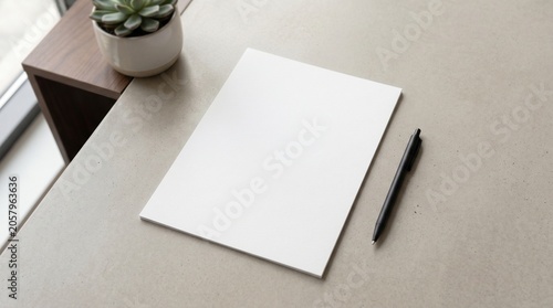 Top view of blank white A4 paper mockup with black pen and small potted plant on grey stone desk background.