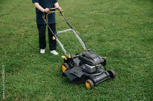 Canvastavla young woman using black and yellow lawn mower for lawn mowing, green grass, sunn