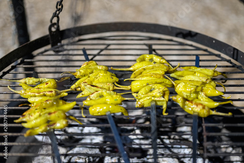 , Deutschland, 13.06.2026, Grüne Peperoni auf einem Grillrost über glühender Holzkohle. Die mediterranen Bratpaprika zeigen erste Röstaromen und werden im Freien über offenem Feuer zubereitet.
