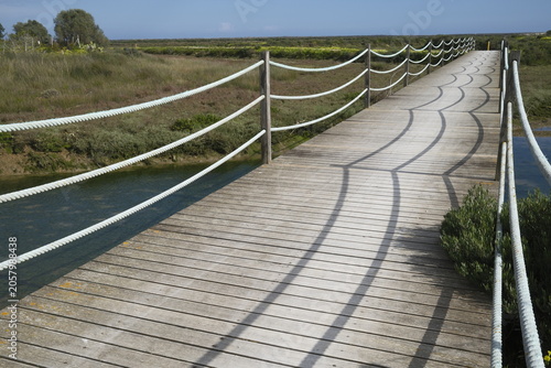 Timber bridge across water in the Ria Formosa Natural Park (Parque Natural da Ria Formosa), Tavira, portugal. Strong shadows run across the timber slats.