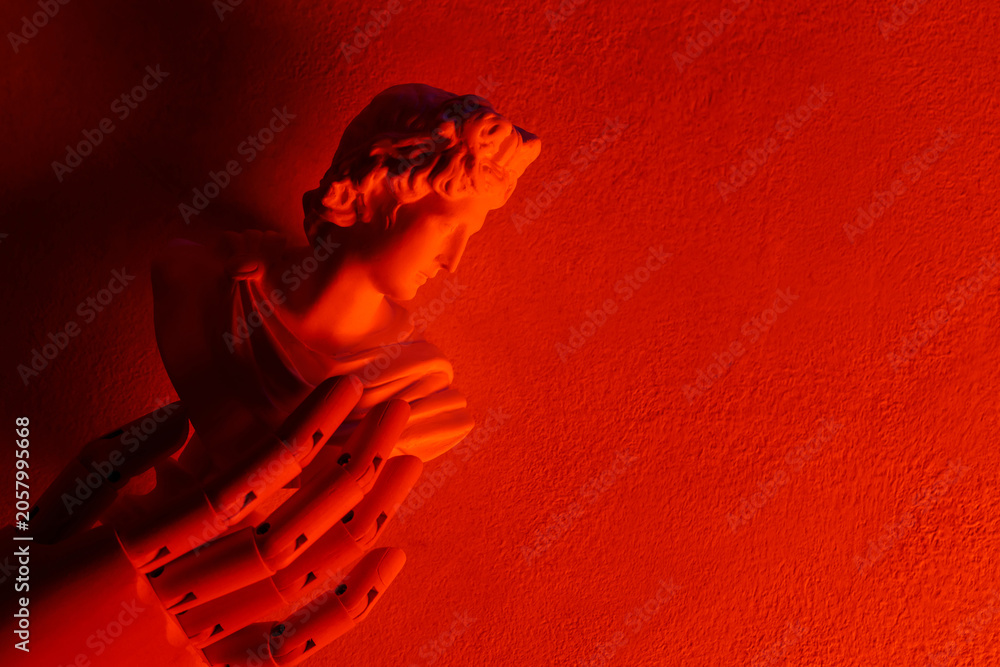 Obraz premium Classical angel statue with praying hands illuminated by dramatic red lighting on textured wall