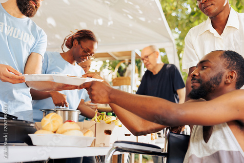 Obraz na płótnie Helpful guy volunteer aids and provides free food to a poor needy african american man in wheelchair