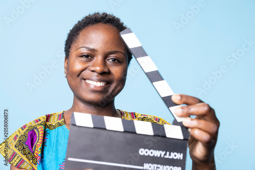 Quadro em tela African American woman working in movie industry with a clapperboard, smiling and using film slate to cut scenes in front of camera, female person in cinematography entertainment