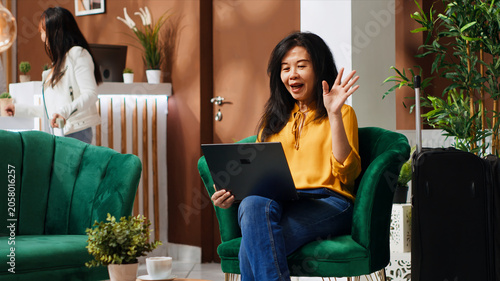 Canvastavla Hotel client waving on video call connection with friends, talking to people after long international flight, woman using laptop network to attend online teleconference remotely on trip