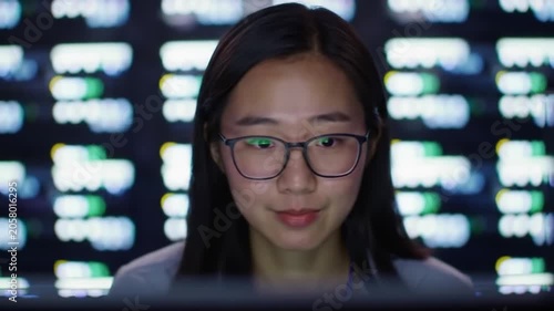 Asian woman with glasses analyzing digital data screen.