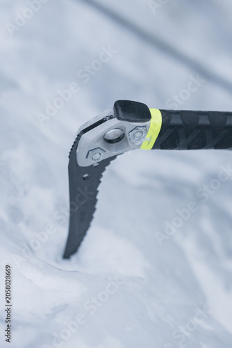 Close-up of modern ice axe pick embedded in snow surface, mountaineering and alpine climbing equipment with serrated blade and carbon fiber handle