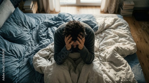 Man Sitting In Bed Holding His Head In Despair