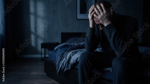 Man Sitting On Bed In Darkness With Hands On Head Clutching Hair