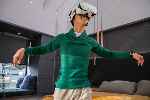 White VR headset is resting on low bed near window seat in modern bedroom featuring rooftops