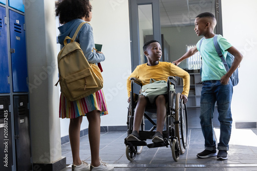 African American children chatting in hallway by blue lockers wheelchair in yellow with green bag