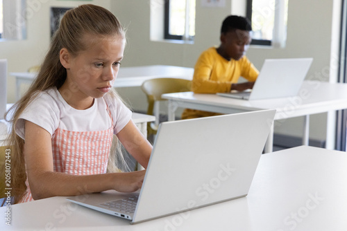 Photos Diverse child classmates working on silver laptops in classroom, girl wearing pi