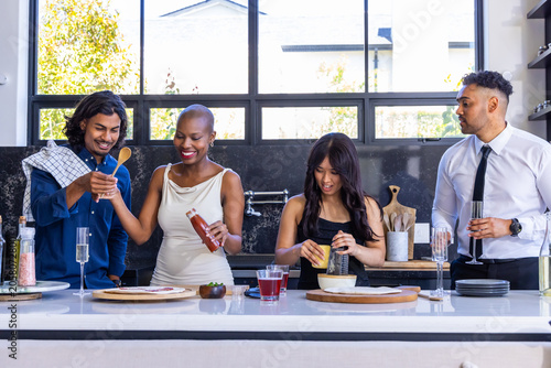 Diverse friends chopping, seasoning and grating at kitchen island with squeeze bottle and flute
