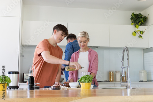 Housemates preparing dinner in modern kitchen, youth pouring olive oil from glass bottle