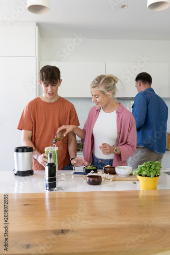 Family parents and teenage son preparing smoothie at kitchen island, pouring oil into blender cup