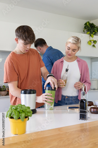 Family with teenage son preparing food while teen securing personal blender cup at kitchen island