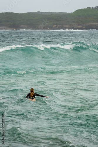 Female surfer paddling out into ocean waves near headland