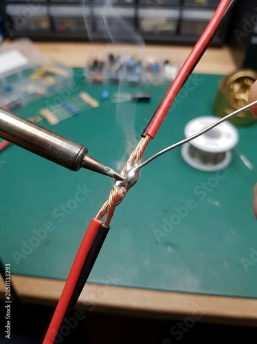 Macro closeup of soldering iron tip joining twisted copper wire strands with solder smoke fumes on green cutting mat electronics workshop DIY repair