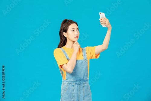 Foto Thoughtful young woman taking selfie with smartphone on blue background
