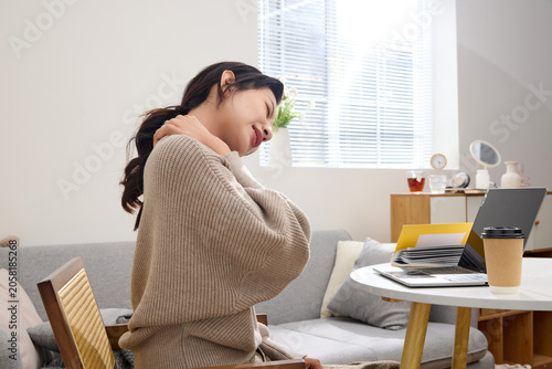 Fotografie Young woman relieving neck pain during work break at home office