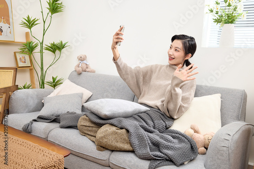 Foto Young woman waving during smartphone video call on sofa at home