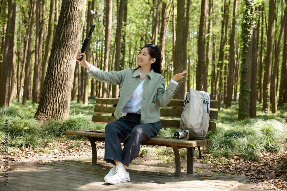 Fototapeta premium Young woman taking selfie on bench in forest park