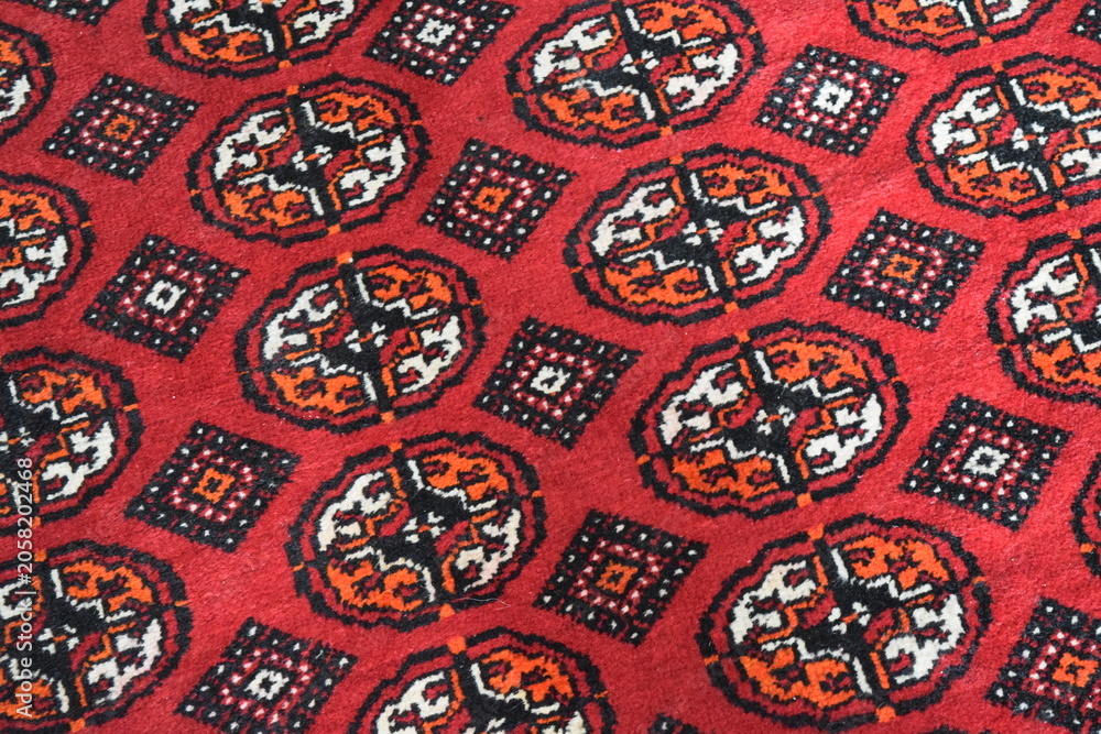 Naklejka premium Close up of a traditional Turkmen handmade wool carpet with authentic red and black geometric patterns. Geometric tribal ornament texture on an oriental nomadic rug, central asian textile art. 