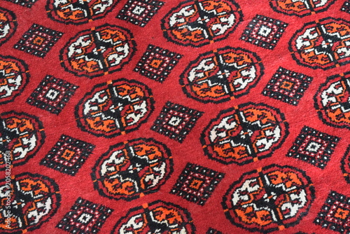Close up of a traditional Turkmen handmade wool carpet with authentic red and black geometric patterns. Geometric tribal ornament texture on an oriental nomadic rug, central asian textile art. 