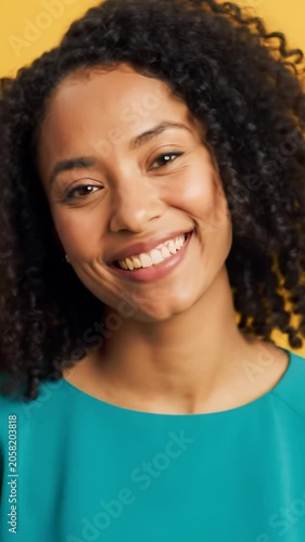 A vibrant young woman in a modern top smiles genuinely in an upper body close-up video against a bright yellow bokeh background, conveying pure joy and positive well-being