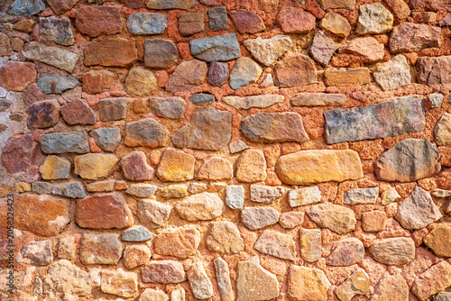 Fotografie Detailed close-up of a traditional stone masonry wall featuring irregular natural rocks embedded in reddish clay mortar