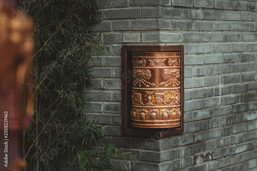 Obraz na płótnie A traditional Buddhist prayer wheel adorns the corner of a dark gray brick wall within a serene Chinese garden