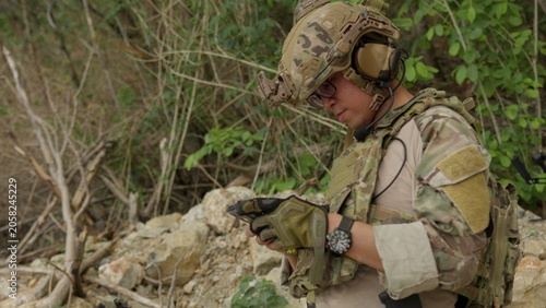 Foto A modern soldier in full tactical gear uses a device for mission coordination and situational awareness while deployed in a rugged, remote outdoor environment