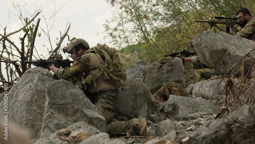 Obraz na plátne Special forces soldiers in full combat gear take defensive positions behind rocks, aiming their rifles during a tactical reconnaissance mission in hostile territory