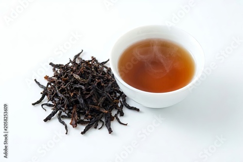Dried black tea leaves and a Chinese teacup on a white background