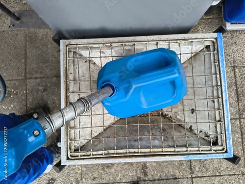 Close-up of a fuel nozzle filling up a blue plastic jerry can at a gas station