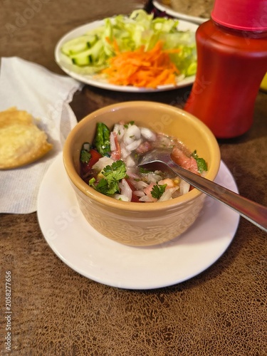 Close-up of fresh Chilean pebre sauce in a ceramic bowl with a metal spoon inside