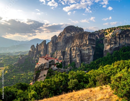 A serene monastery perched atop a rugged cliff surrounded by lush greenery under a blue sky with scattered clouds