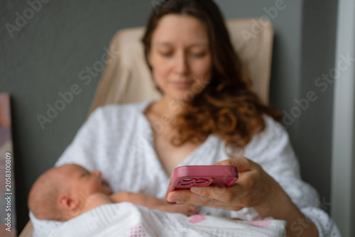 New mother balancing childcare and technology, cradling her sleeping newborn baby while engaging with a smartphone, representing modern parenting in the digital age