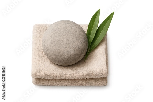 Smooth gray spa stone on folded beige towel with green leaf