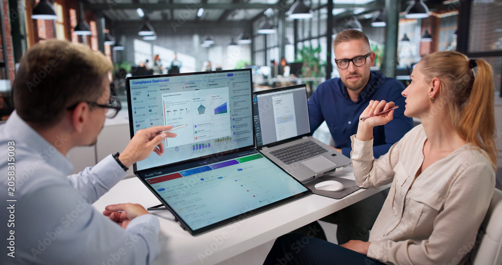 Naklejka premium Diverse Team Reviews Compliance Data Together Using Laptop