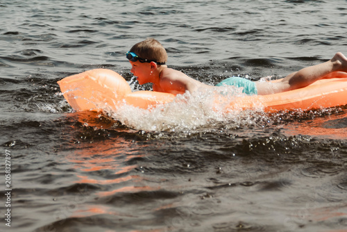 Fotografie little boy joyfully plays orange inflatable mattress river, creating bright splashes around him