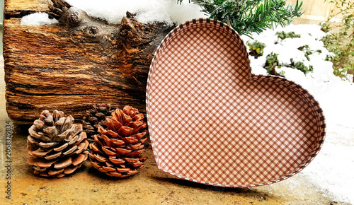 Foto Horizontal View of Heart Shaped Box Lid Beside Pine Cones and Snow Dusted Log Ou