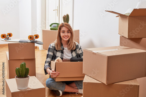 Smiling woman sitting among moving boxes in new apartment