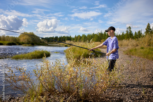Photos A smiling teenage boy enjoys fishing on a scenic riverbank during a sunny day