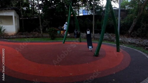 Empty park playground with red and black ground and swing set structures
