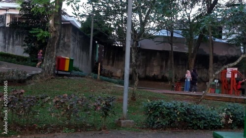 People walking and playing in a public park with swings and green trees
