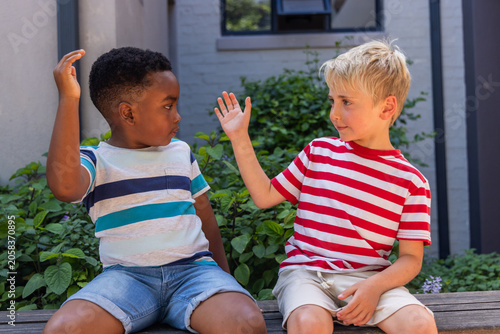 Foto Diverse male school-age friends sitting on wooden bench by hedge, wearing stripe