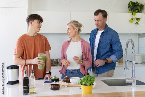 Family parents with teenage son preparing green smoothie and chopping vegetables at kitchen island