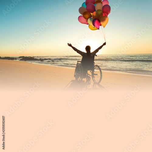 A person in a wheelchair holding a bunch of colorful balloons, arms outstretched towards the sky, standing on a beach with the ocean and sunset in the background